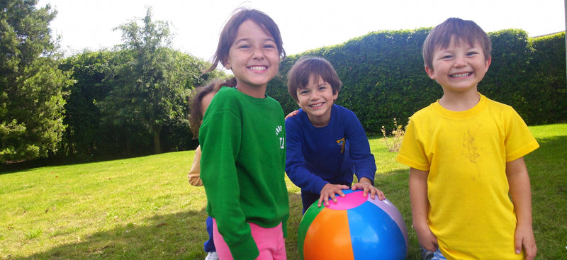 Drie lachende kinderen spelen met een bal in de tuin
