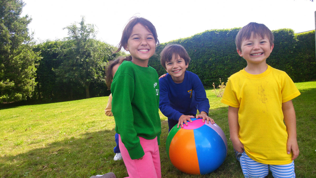 Drei lachende Kinder spielen mit einem großen Wasserball im Gras